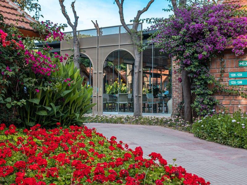 Pad tussen tuin met rode bloemen naar gebouwentree onder blauwe lucht