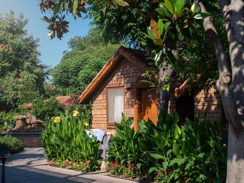 Gezellig houten huisje omgeven door weelderig groen en bloemen onder een heldere hemel.