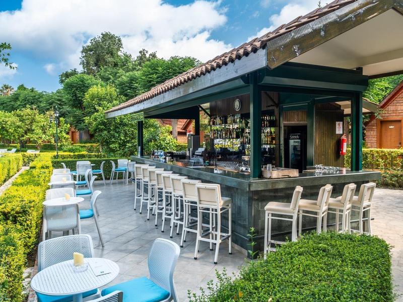 Moderne buitenbar met zitplaatsen en groene haag onder blauwe lucht.