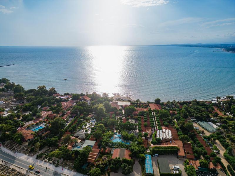 Zonnige kustlandschap met groen, gebouwen en kalme zee op de achtergrond.