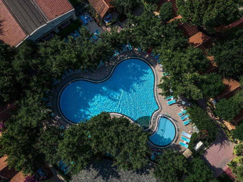 Een hartvormig zwembad omgeven door weelderig groen en ligstoelen.