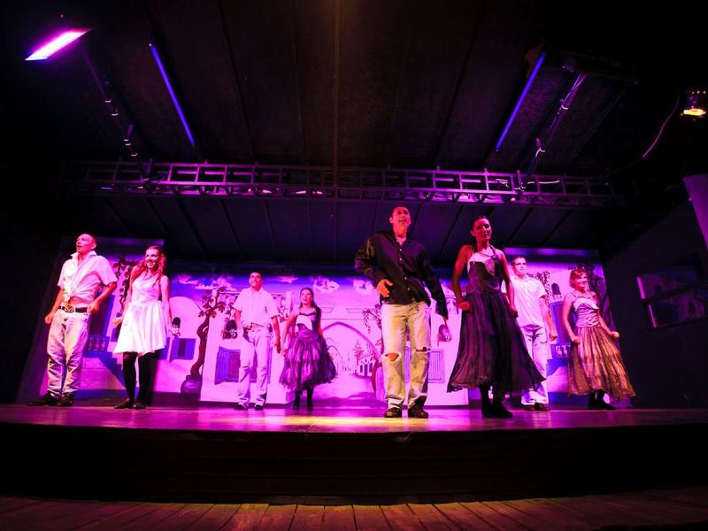 Zes mensen dansen en poseren op een podium met kleurrijke verlichting.