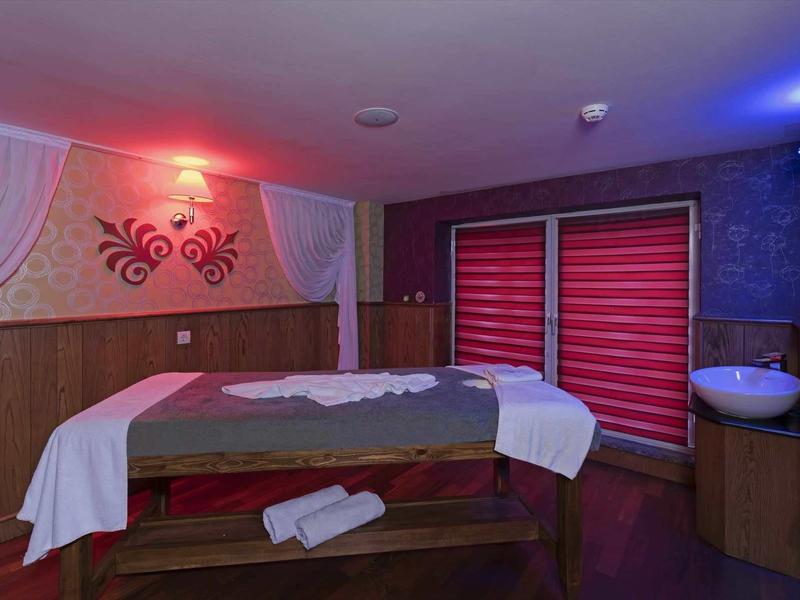 Sala massaggi con lettino in legno, asciugamani bianchi e luce soffusa.