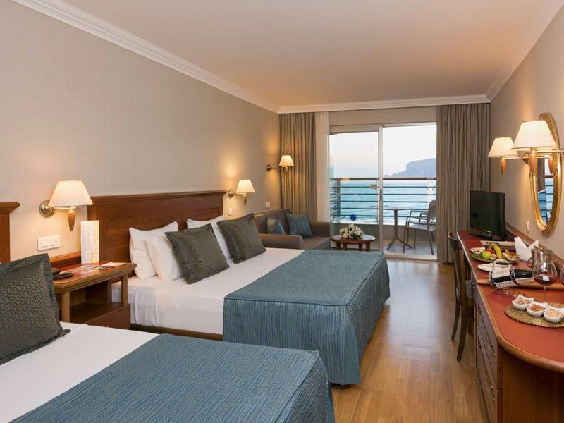 Camera d'hotel moderna con due letti, arredi neutri e balcone con vista mare.