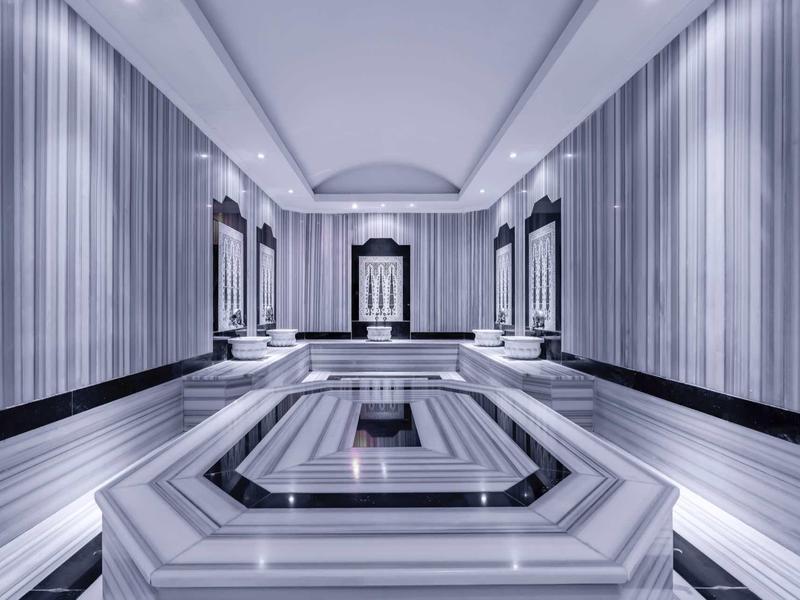 Interno elegante con pareti a righe e grande vasca centrale in marmo, probabilmente spa.