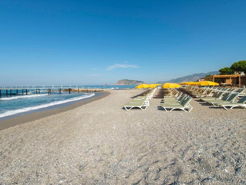 Spiaggia di ciottoli con sdraio e ombrelloni gialli sotto un cielo azzurro.
