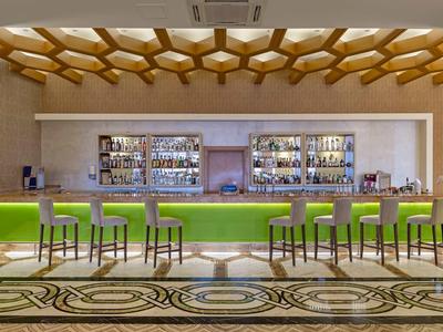 Bar moderno con sgabelli verdi e soffitto a motivi geometrici in legno.