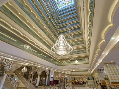 Interno di un hotel di lusso con grande lampadario e più piani sotto una copertura in vetro.