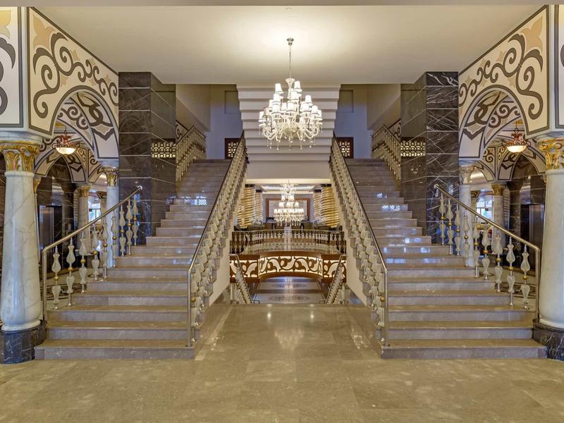 Atrio di hotel di lusso con grande scala in marmo e lampadario elegante.