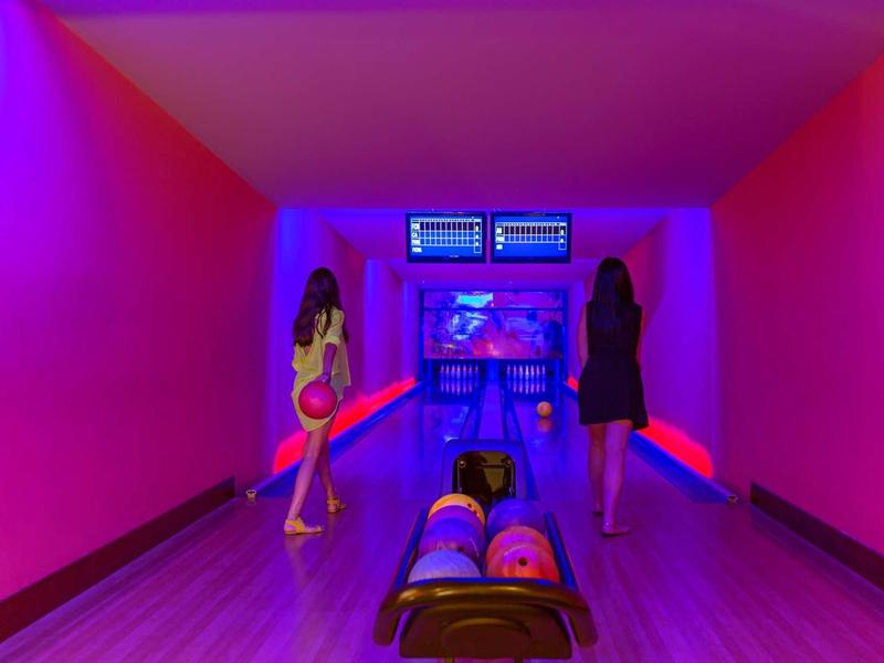 Due donne giocano a bowling in una corsia illuminata di viola e blu.