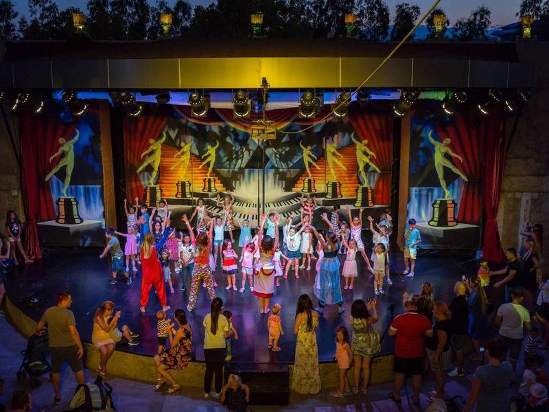 Spettacolo notturno all'aperto con ballerini e pubblico sotto un tetto illuminato.