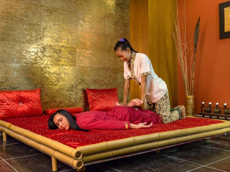Massaggio rilassante in una stanza accogliente con letto in bambù e cuscini rossi.
