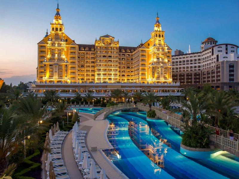 Hotel di lusso illuminato con piscina esterna e palme al tramonto.