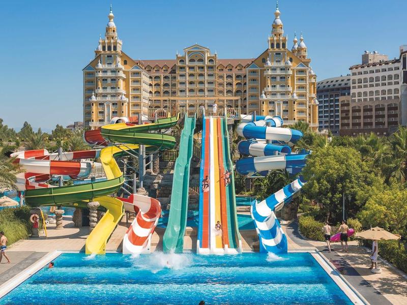 Grande hotel con scivoli d'acqua colorati che conducono a una piscina luminosa.