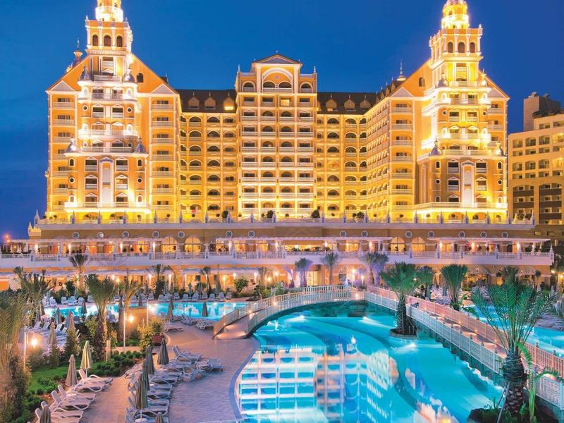 Grande hotel illuminato di notte con piscina all'aperto e lettini.