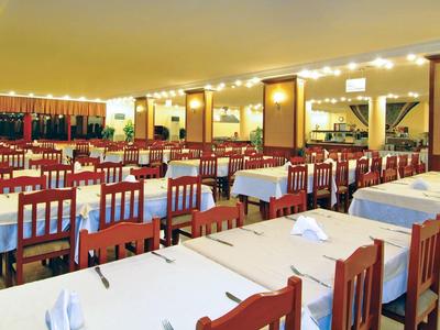 Ampia sala da pranzo con molti tavoli e sedie, apparecchiata con tovaglie bianche e ben illuminata.