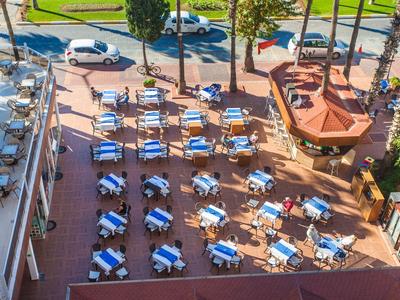 Terrazza dell'hotel soleggiata con tavoli e sedie circondata da alberi e parcheggi.