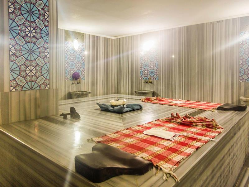 Sala hammam moderna con letti in marmo riscaldati e finestre ad arco decorative.