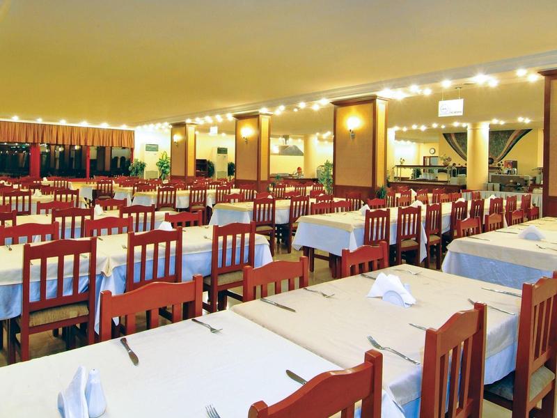 Ampia sala da pranzo con molti tavoli e sedie, apparecchiata con tovaglie bianche e ben illuminata.