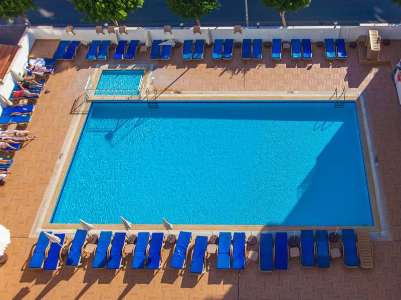 Piscina rettangolare all'aperto con lettini blu e ombrelloni su terrazza beige.