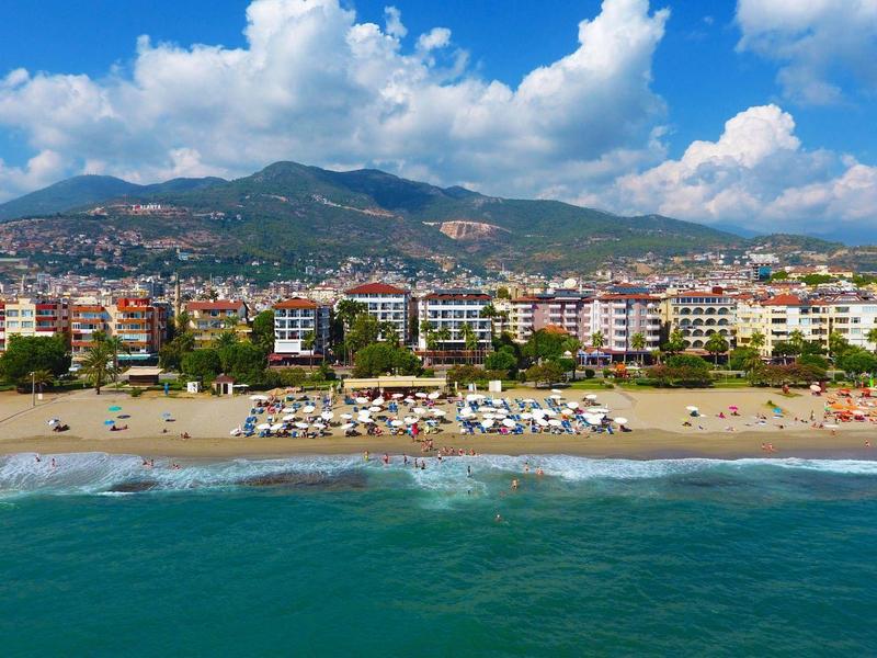 Spiaggia con hotel e montagne sullo sfondo sotto un cielo azzurro con nuvole.