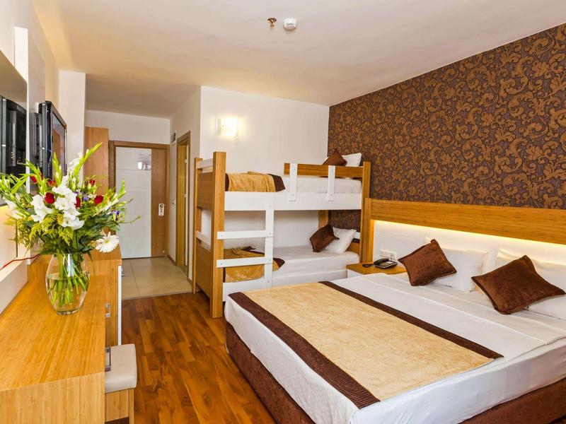 Camera d'hotel accogliente con letto matrimoniale e letto a castello, pavimento in legno e fiori sul tavolo.