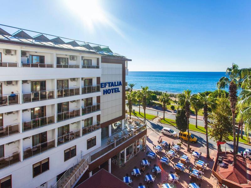 Hotel con camere con balcone, area piscina e vista sul mare in una giornata di sole.