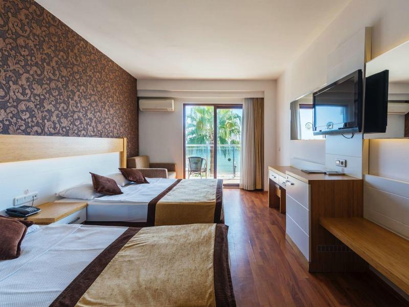 Camera d'hotel luminosa con due letti singoli, pavimento in legno e balcone con vista sul mare.