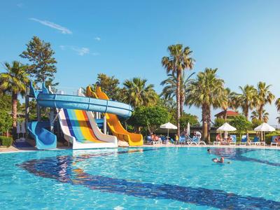Großer Pool mit runden Wasserrutschen in Blau, Gelb und Orange, umgeben von Palmen und Sonnenschirmen.