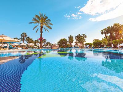 Großer blauer Pool mit Palmen, Sonnenschirmen und Liegestühlen unter blauem Himmel.