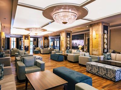 Großer, eleganter Lounge-Bereich mit Polstersesseln, Sofas, Holzboden und Kronleuchter an der Decke.