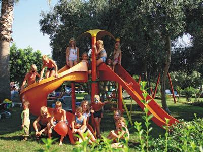 Kinder spielen auf einem roten Spielplatz mit Rutsche im grünen Park bei Sonnenschein.