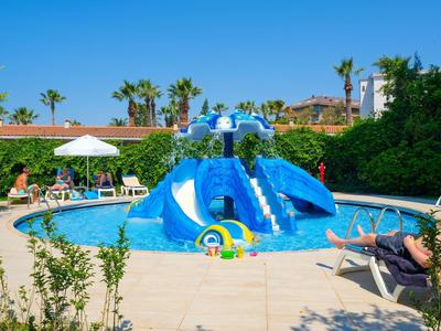 Ein blauer Wasserspielplatz mit Rutschen im runden Pool, umgeben von Liegestühlen und grünen Pflanzen.