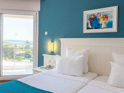 Brightly furnished hotel room with two beds and access to a balcony overlooking the sea.