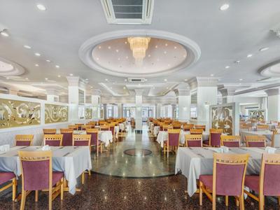 Großer, eleganter Speisesaal mit gedeckten Tischen, Holzmöbeln und hellem Deckenlicht.