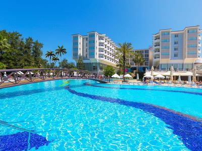 Großer Hotelpool mit klar blauem Wasser und Sonnenschirmen, umgeben von Palmen und mehrstöckigen Gebäuden.