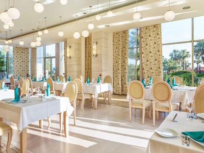 Helles Hotelrestaurant mit großen Fenstern, weißen Tischen und klassischen Stühlen mit blauer Polsterung.