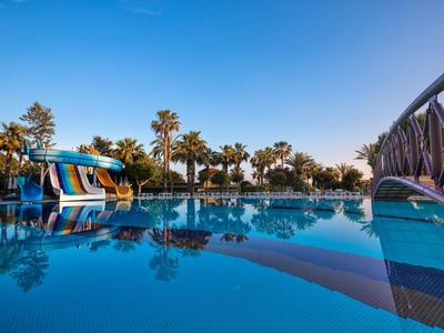 Ein klarer Pool mit Wasserrutsche und Palmen bei sonnigem Himmel in einem Urlaubsort.