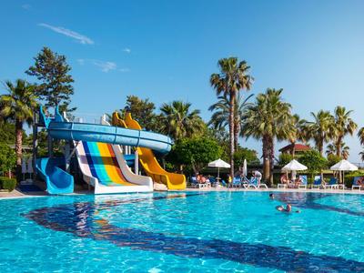 Hotelpool mit bunten Wasserrutschen, umgeben von Palmen und Sonnenschirmen bei klarem Himmel.