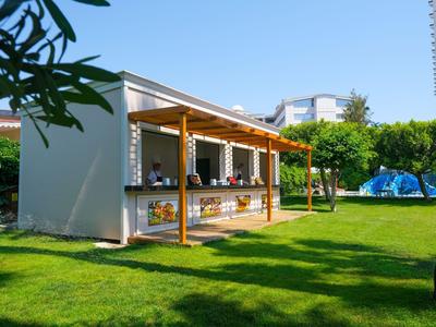 Kleiner Außenkiosk mit Holzüberdachung auf gepflegtem Rasen bei klarem Himmel.