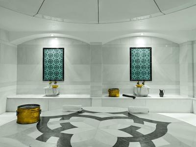 Modernes weißes Hamam mit Mosaikfliesen, goldenen Behältern und grauem Steinboden.