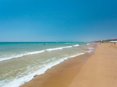 Leerer Sandstrand mit sanften Wellen unter klarem blauem Himmel an der Küste.