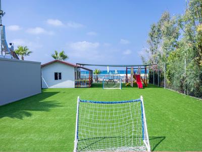 Grüner Kunstrasen mit Fußballtor, Spielplatz und Blick auf den Pool in einem Urlaubshotel.