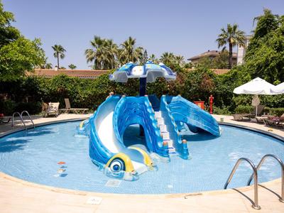 Blauer Kinderrutschen-Spielbereich in einem runden Hotelpool umgeben von Palmen und Sonnenschirmen.