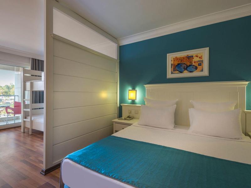 Camera d'hotel moderna con letto matrimoniale, parete blu, lampade da comodino e balcone con vista mare.