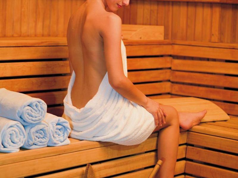Donna avvolta in asciugamano seduta su panca di legno in sauna con secchio.