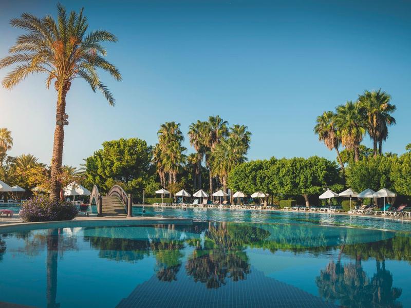Grande piscina dell'hotel con palme e ombrelloni sotto un cielo limpido.