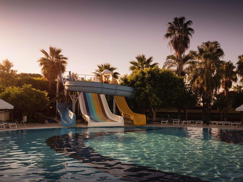 Piscina con scivoli colorati e palme al tramonto in un hotel.