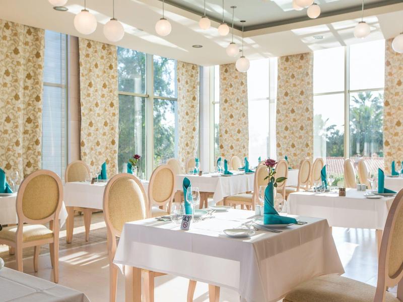 Ristorante luminoso con grandi finestre, tavoli bianchi e sedie eleganti alla luce del giorno.