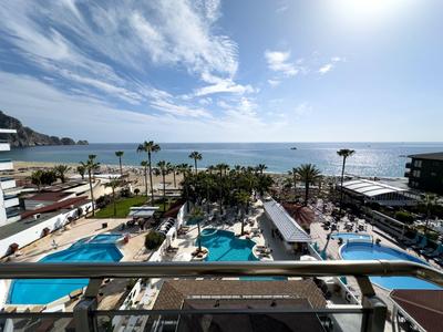 Vista di più piscine e palme con il mare sullo sfondo in una giornata di sole.